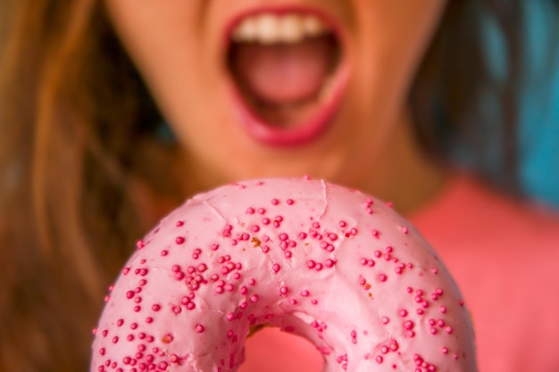 A woman with pink lips is holding a pink donut with sprinkles on it.