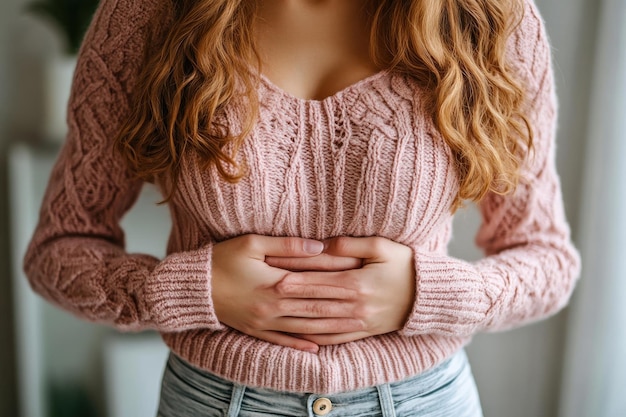 Photo a woman with a pink sweater and jeans is holding her stomach