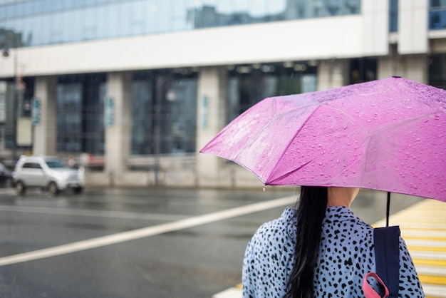 Woman with a pink umbrella in rainy weather on the city background. Rainy day. City street style.