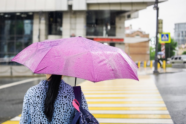 Woman with a pink umbrella in rainy weather crossing the pedestrian.