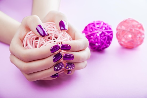 Woman with purple manicure holds a ball on pink background Nail art design