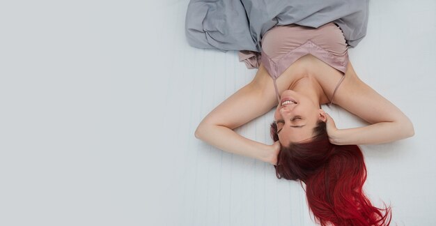 Woman with red hair wakes up smiling in bed stretches