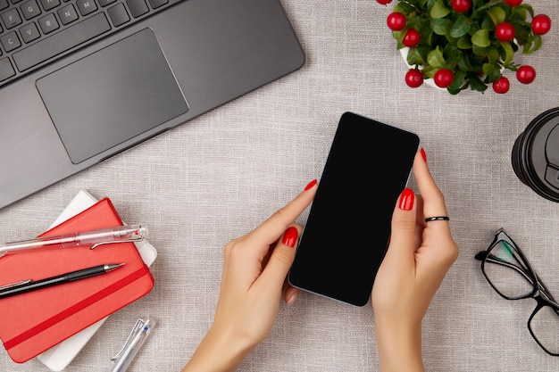 Woman with red manicure holding mobile phone on gray table