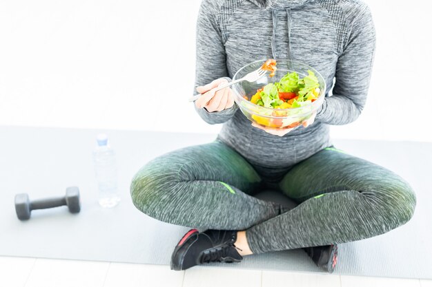 Woman with salad and a dumbbell sitting on the floor