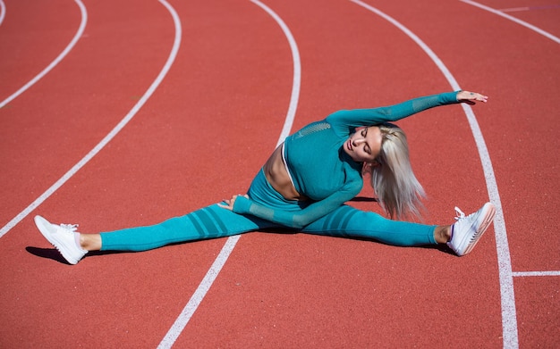 Woman with sexy fitness body in sportswear stretching on stadium, split.