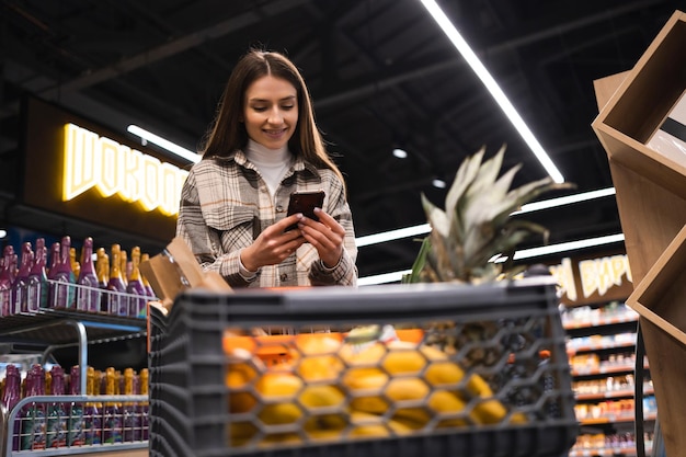 Woman with shopping trolley looking at shopping list in smartphone