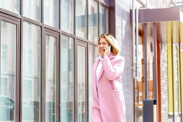 A woman with short brown hair walks around the city and talks on the phone in the spring