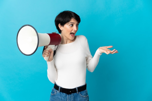 Woman with short hair over isolated space holding a megaphone and with surprise facial expression