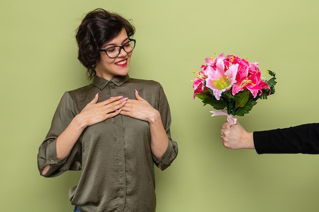 Photo woman with short hair looking pleased and happy while receiving bouquet of flowers from her boyfriend celebrating international women's day march 8 standing over green background