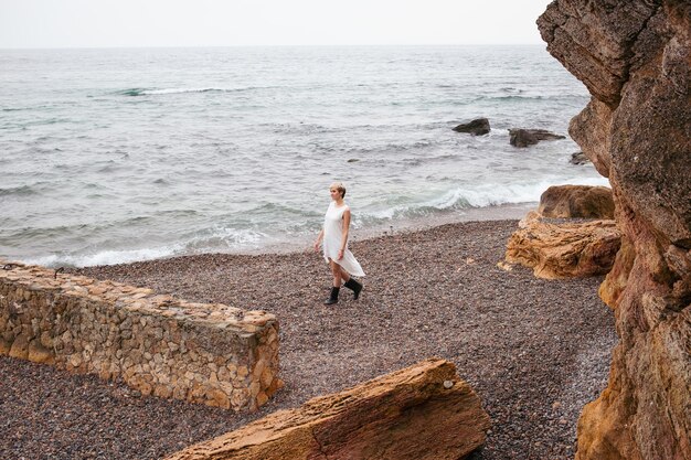 Woman with short haircut wearing dress near sea and rocks in autumn