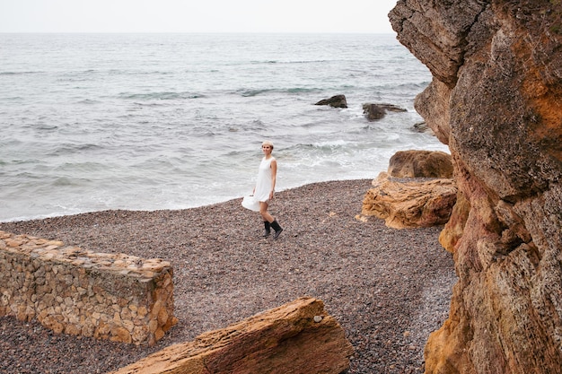 Woman with short haircut wearing dress near sea and rocks in autumn