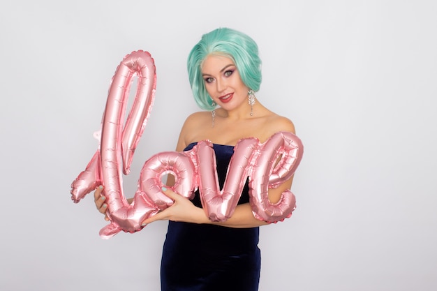 Woman with short mint hair in dark blue velvet dress holding balloon with word LOVE