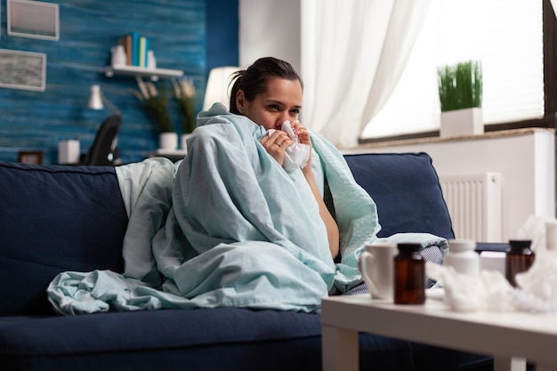 Woman with sickness wrapped in blanket at home ill feeling unwell young caucasian adult suffering fr...