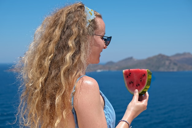 Woman with a slice of watermelon in a straw hat near the sea