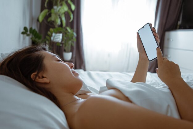 Woman with smartphone in bed with white sheets