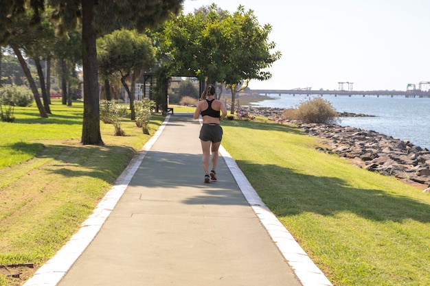 Woman with sportswear, running along the side of the river. View from behind. Fit woman concept.