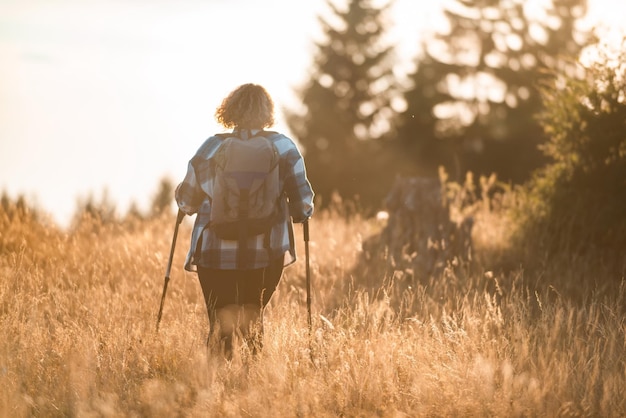 A woman with sticks a backpack on her back and mountaineering equipment walking on top of a mountain at sunset