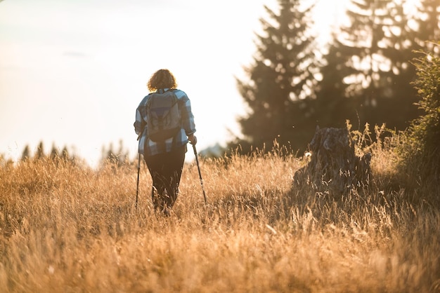 A woman with sticks a backpack on her back and mountaineering equipment walking on top of a mountain at sunset