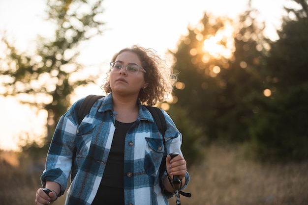 A woman with sticks a backpack on her back and mountaineering equipment walking on top of a mountain at sunset