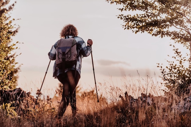 A woman with sticks a backpack on her back and mountaineering equipment walking on top of a mountain at sunset