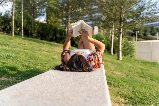 Photo woman with sunglasses enjoying reading a book while relaxing in a park