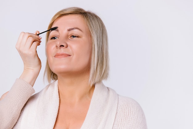 A woman with a sweet smile and gentle makeup on a white background. The hand of the master corrects the eyebrows with a brush. High quality photo