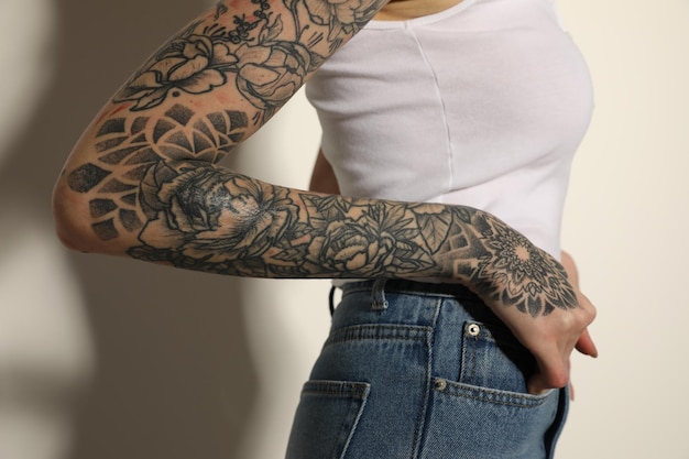 Photo woman with tattoos on arm against light background closeup