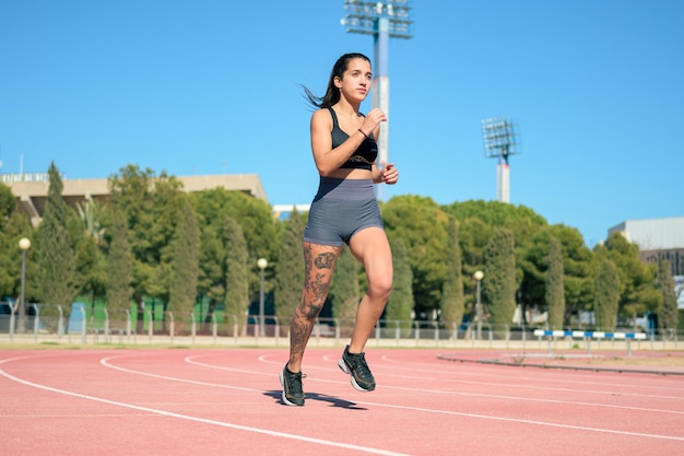 Woman with tattoos running on athletic track on a sunny day