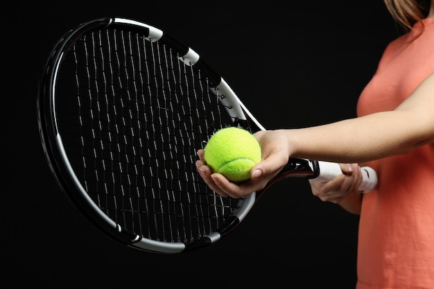 Woman with tennis racket and ball on black background