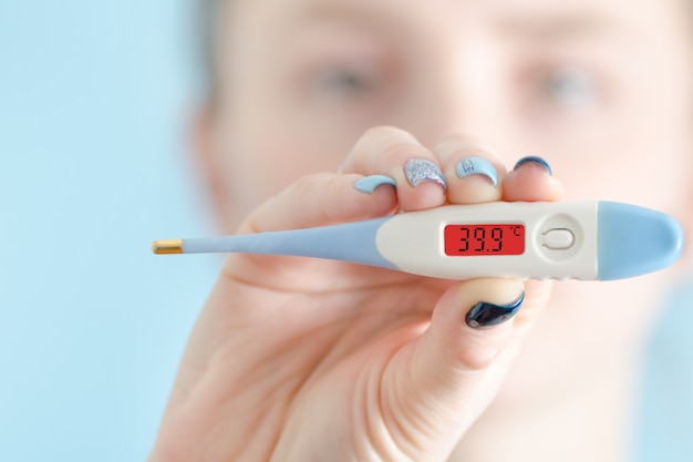 Woman with a thermometer in his hand. Increased body temperature. Face on background