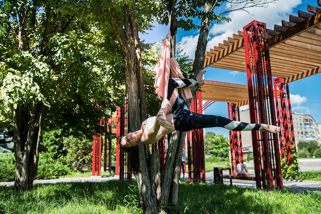 Woman with a thin waist with strong arms engaged in exercises on an air hammock in nature