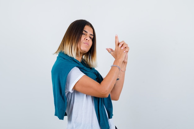 Woman with tied sweater showing gun gesture in white t-shirt and looking proud , front view.