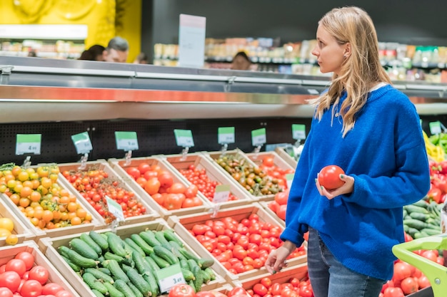 Woman with tomato in hand at the vegetables in the store