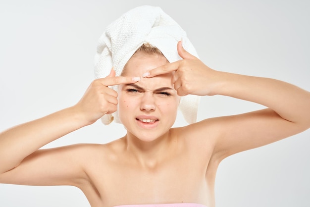 Woman with a towel on her head squeezes out pimples on her face clean skin health