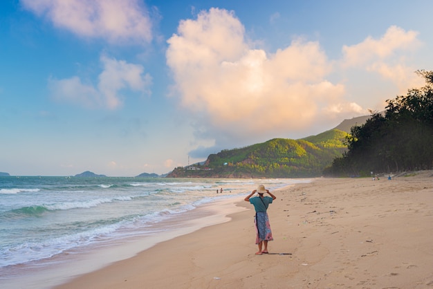 Woman with traditional vietnamese hat looking at view on tropical beach. Quy Hoa Quy Nhon Vietnam travel destination, central coast between Da Nang and Nha Trang