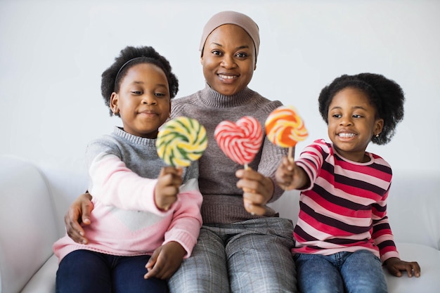 Woman with two daughters holding lollipops on couch