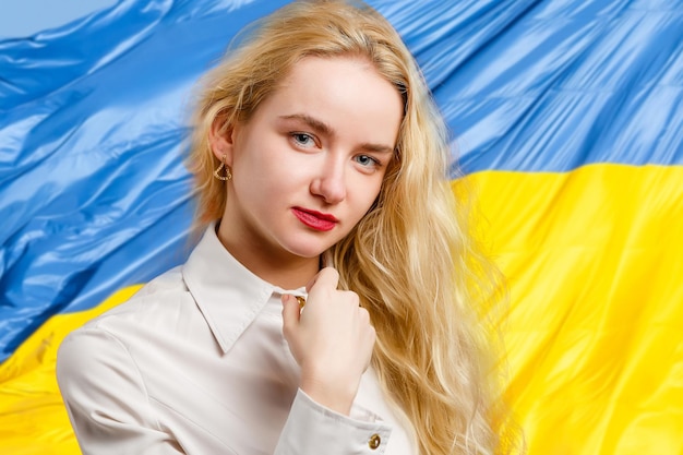 Woman with Ukraine flag at background looking at camera Concept of standing with Ukrainian nation in war with Russia