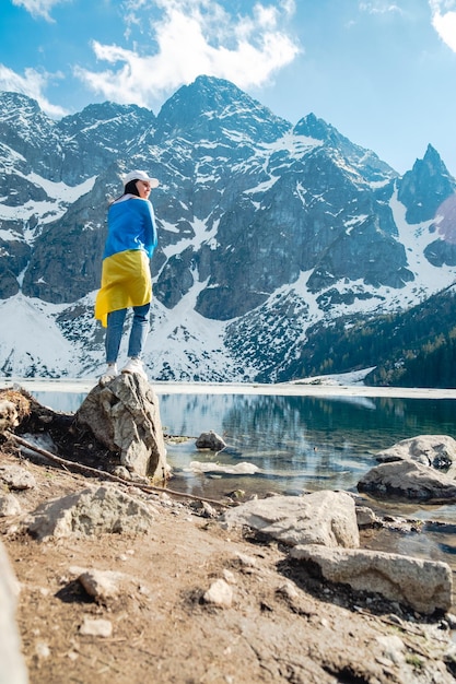 A woman with Ukrainian flag is standing on the shore of a lake Morskie Oko