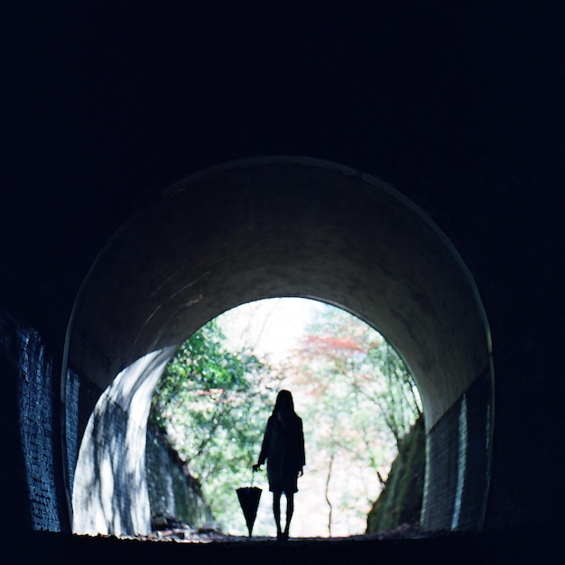 Woman with umbrella standing in tunnel