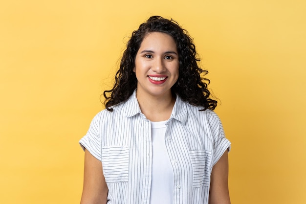 Woman with wavy hair looking at camera with toothy smile expressing happiness being in good mood