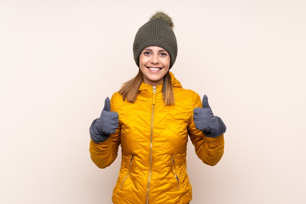 Woman with winter hat over isolated wall giving a thumbs up gesture