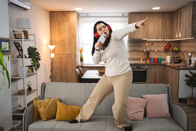 Woman with wireless headphones on sofa singing karaoke at home