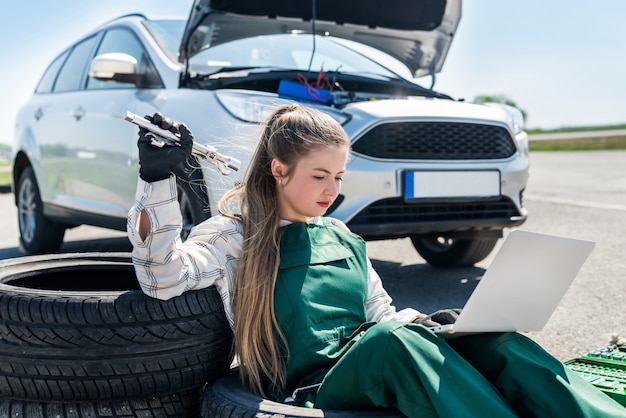 Woman with wrenches and laptop servicing broken car