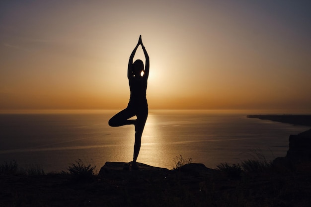 The woman with yoga posture on the mountain at sunset