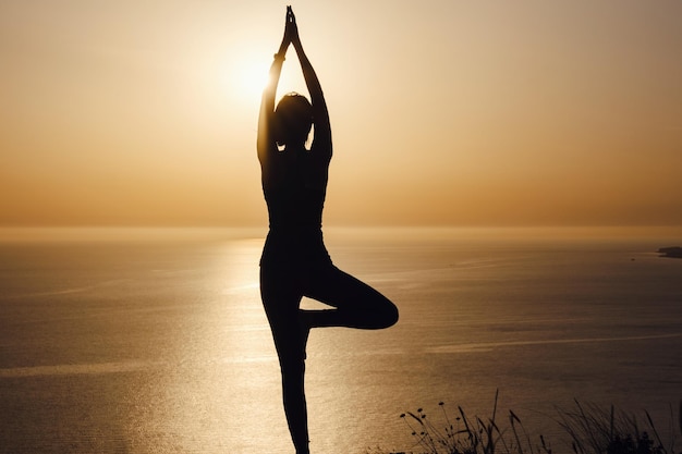 The woman with yoga posture on the mountain at sunset