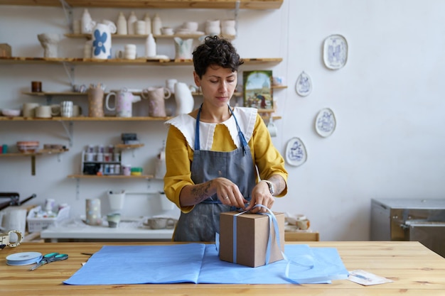 Woman work in craft ceramics store or studio packing pottery in gift box for delivery to consumer