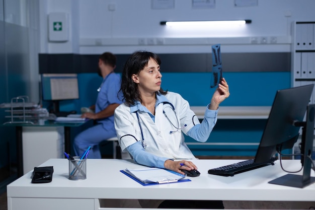 Woman working as doctor analyzing x ray scan results for medical diagnosis and healthcare checkup. Specialist holding radiography for examination and analysis, working late at office