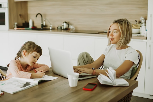 Woman working at home with her little daughter sitting near and drawing