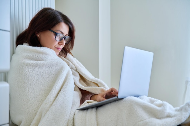 Woman working at home with laptop warming with blanket and heating radiator