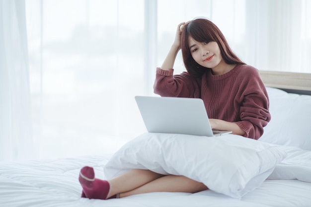 Woman working on a laptop sitting on the bed in the house.